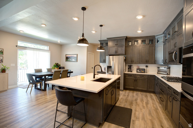 983 South 950 West Provo, UT 84601 - Photo 6 of 56 Contemporary kitchen featuring an island with a breakfast bar, dark cabinetry, stainless steel appliances, and light wood-finish flooring