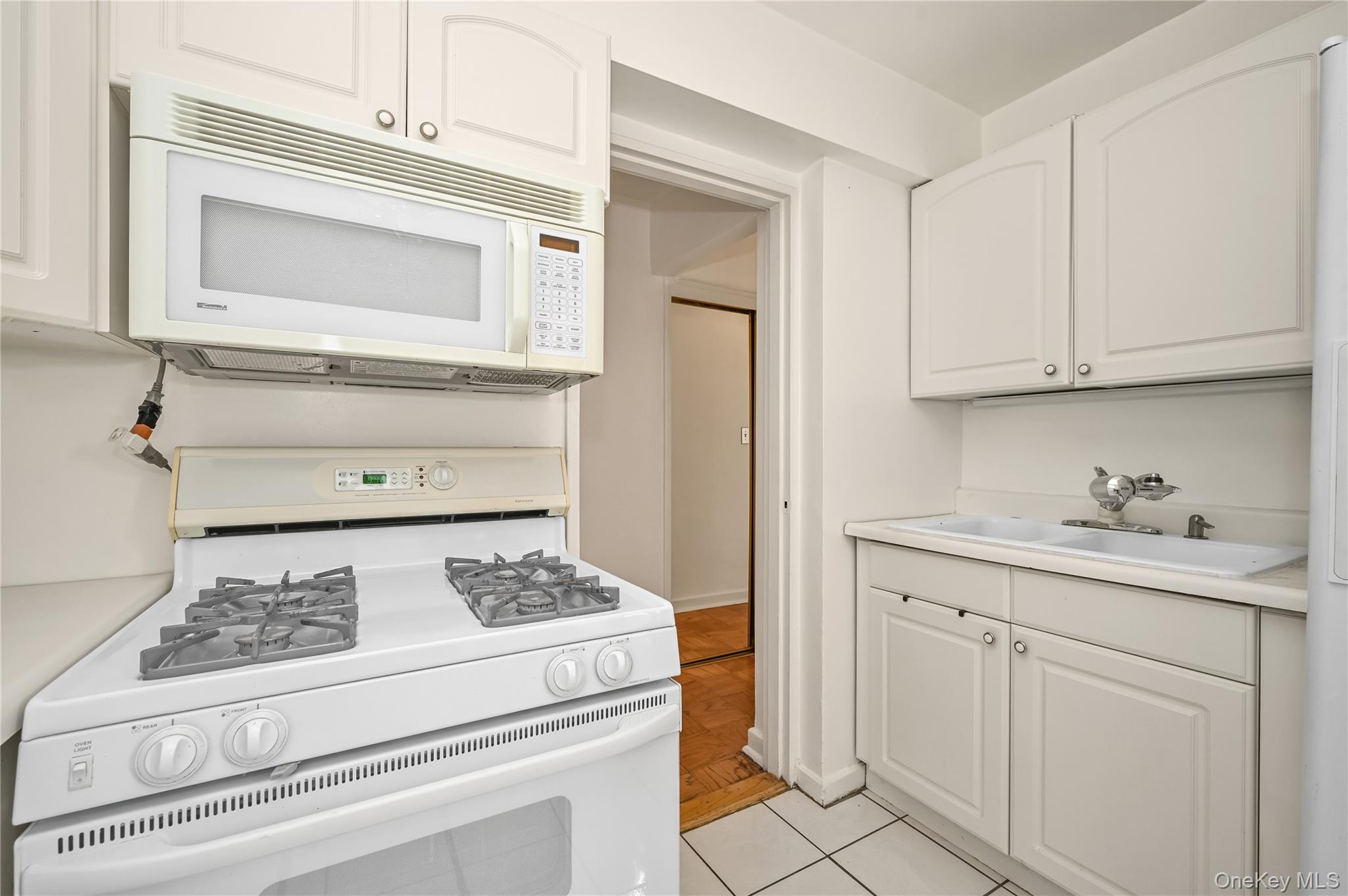 99-10 60th Avenue, Unit 1E Queens, NY 11368 - Photo 12 of 18 a kitchen with white cabinets and appliances