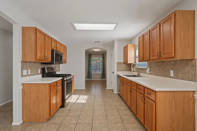 a large kitchen with stainless steel appliances granite countertop a stove top oven a sink dishwasher and a refrigerator with wooden cabinets