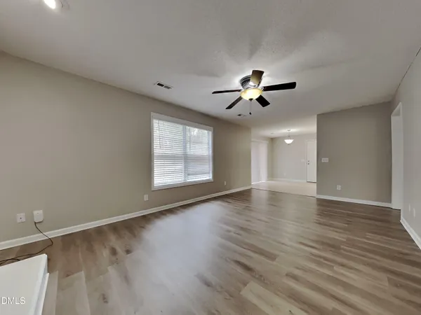an empty room with wooden floor ceiling fan and window