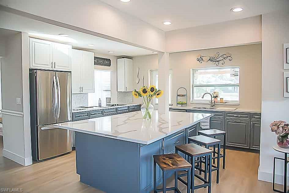 3220 63rd Street Southwest Naples, FL 34105 - Photo 25 of 36 Kitchen featuring a kitchen bar, freestanding refrigerator, a kitchen island, white cabinetry, and light wood-type flooring