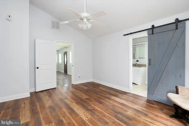 a view of an empty room with wooden floor and a ceiling fan