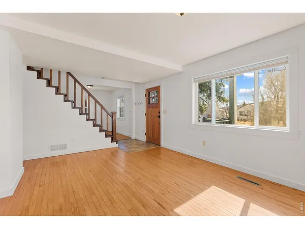 a view of an empty room with wooden floor and windows