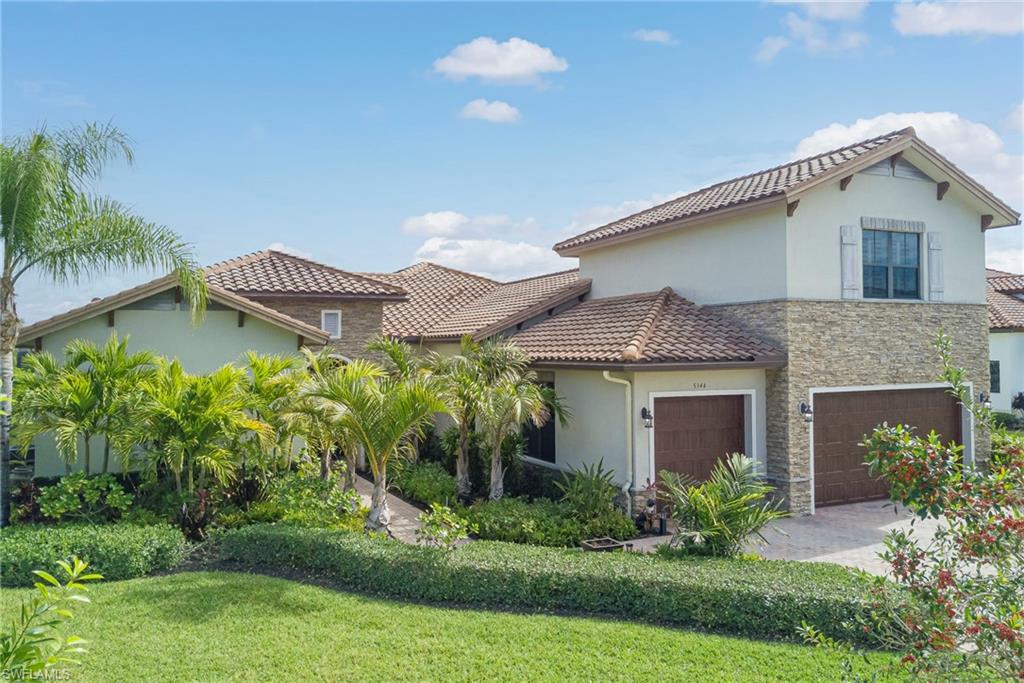 Mediterranean house featuring stucco siding, a front lawn, stone siding, an attached garage, and driveway