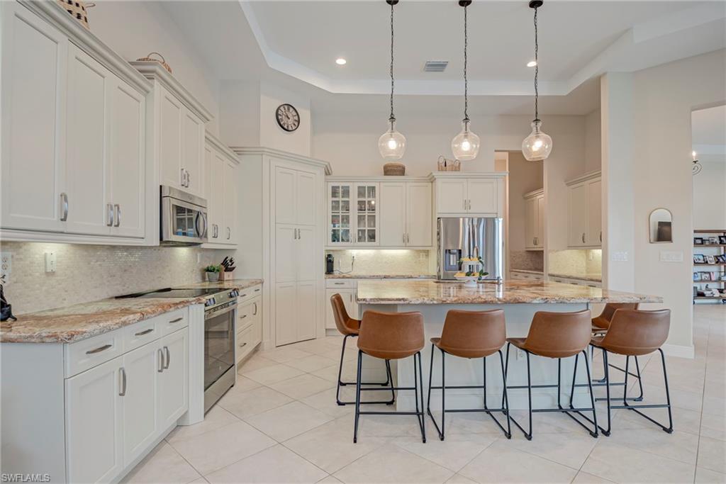 5344 Allen Place Ave Maria, FL 34142 - Photo 9 of 43 Kitchen featuring stainless steel appliances, light stone countertops, a breakfast bar area, decorative backsplash, and a high tray ceiling