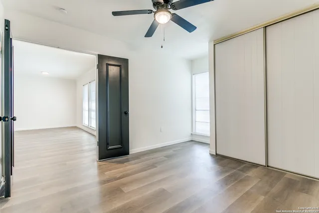 a view of an empty room with wooden floor and a ceiling fan