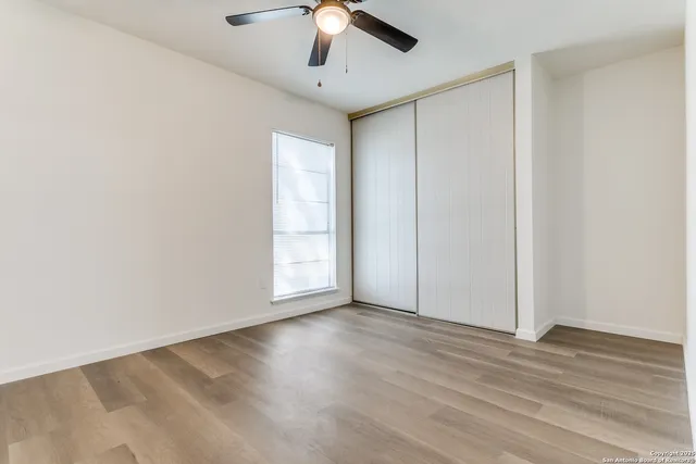 an empty room with wooden floor chandelier fan and windows