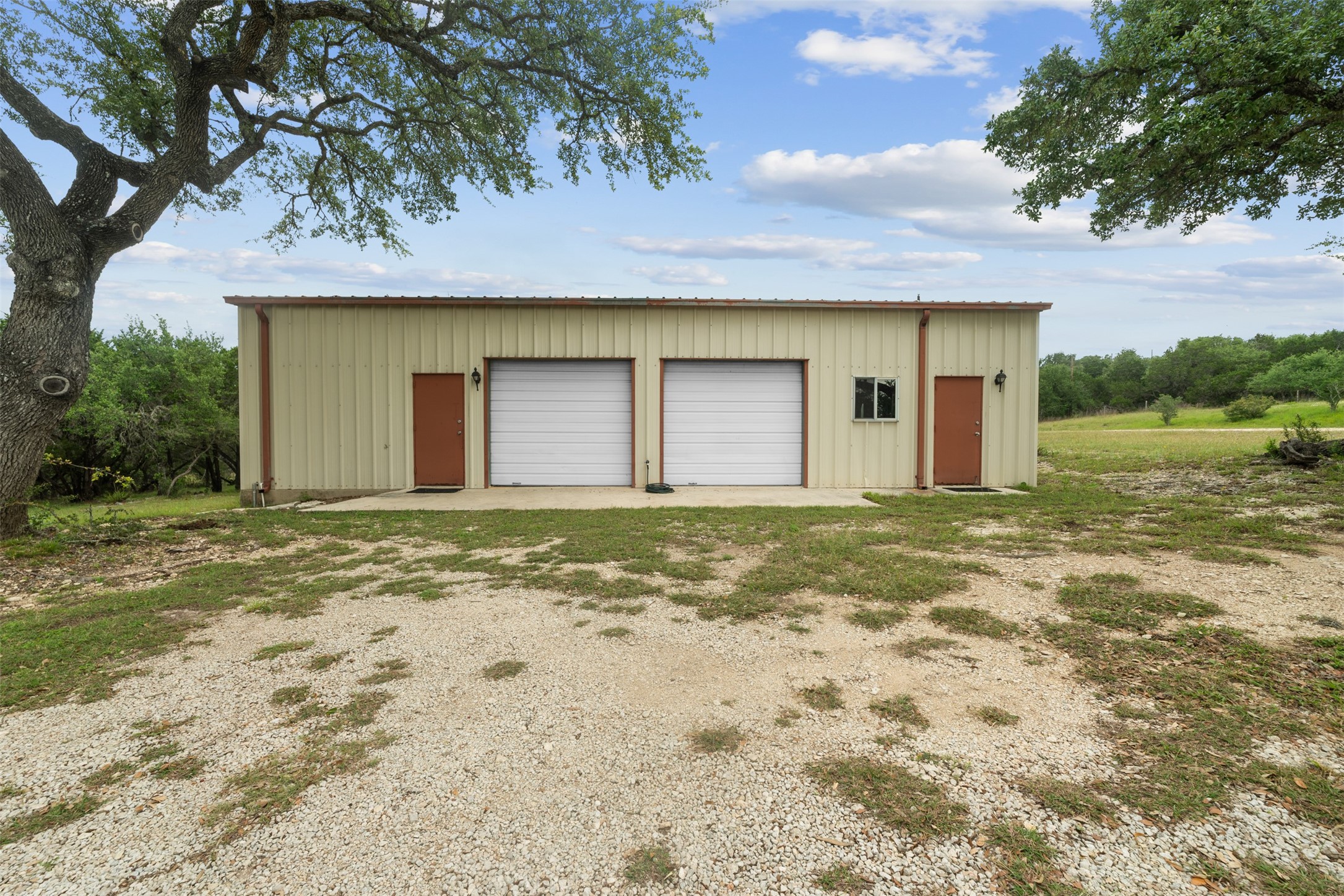 34000 Smithson Valley Road Bulverde, TX 78163 - Photo 40 of 50 Large insulated metal workshop with two roll-up doors, side entries, and ample space for equipment, vehicles, hobbies, or storage. Nestled beneath mature oak trees, it offers both functionality and a scenic Hill Country setting.