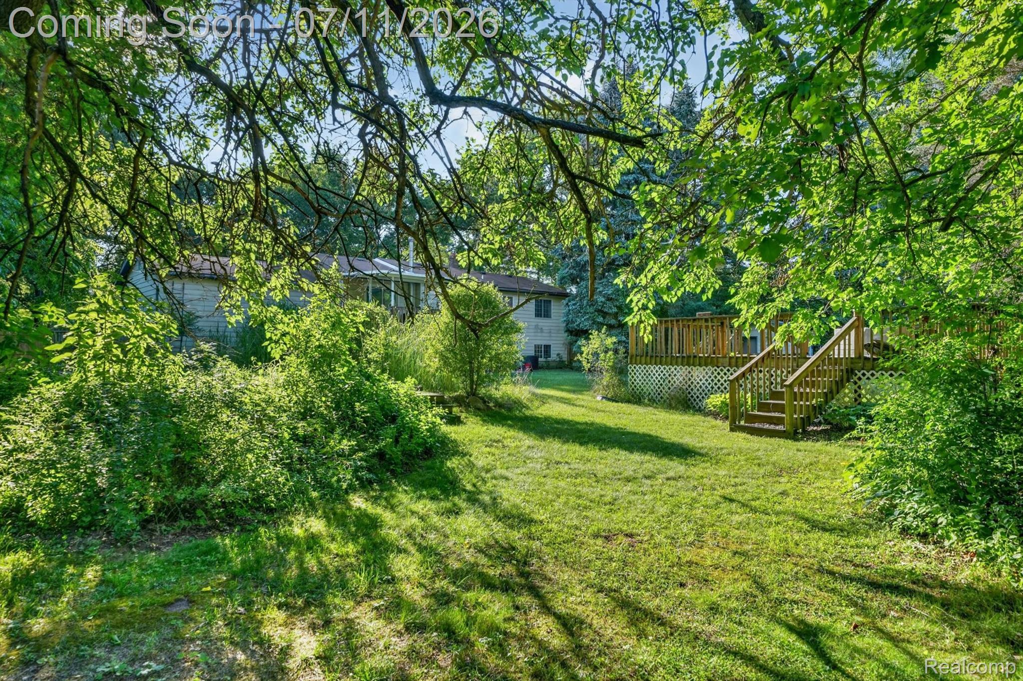 4430 North Center Road Flint, MI 48506 - Photo 45 of 49 Expansive backyard featuring a large wooden deck with railings and steps, a sunroom extension, and mature trees providing natural shade