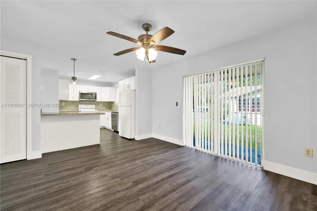a view of an empty room with wooden floor and a kitchen