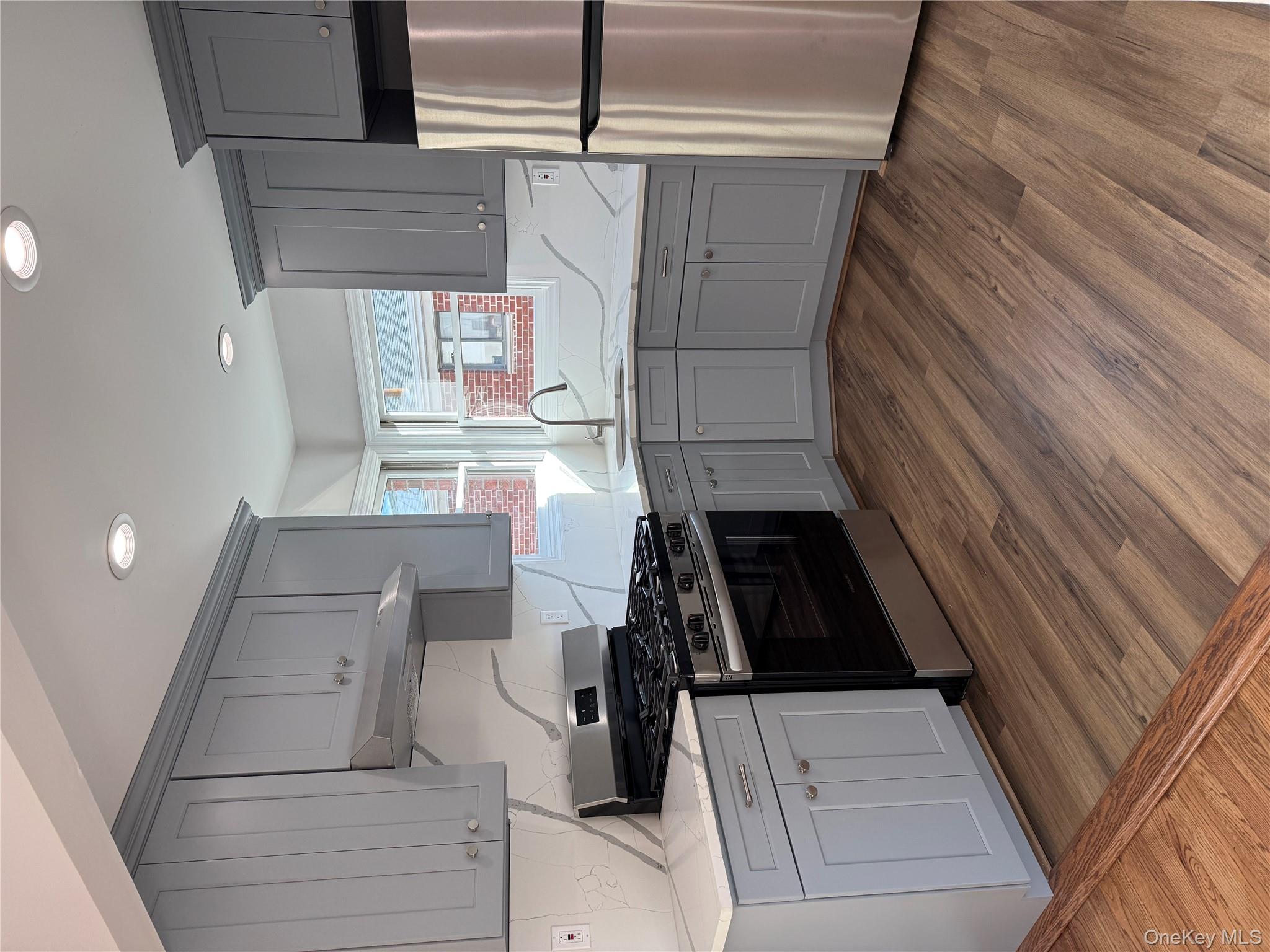 Kitchen with stainless steel range oven, gray cabinets, refrigerator, exhaust hood, and light stone counters