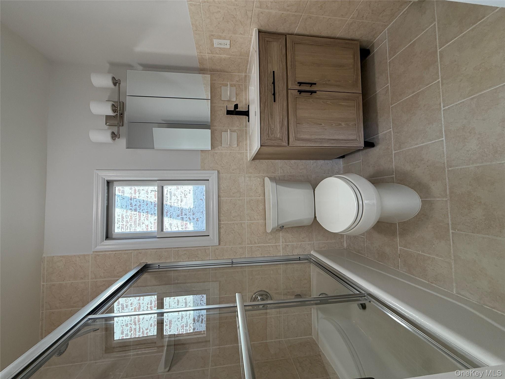 130-09 58th Road Queens, NY 11355 - Photo 13 of 18 Bathroom with tile walls, vanity, enclosed tub / shower combo, light tile patterned floors, and a wainscoted wall