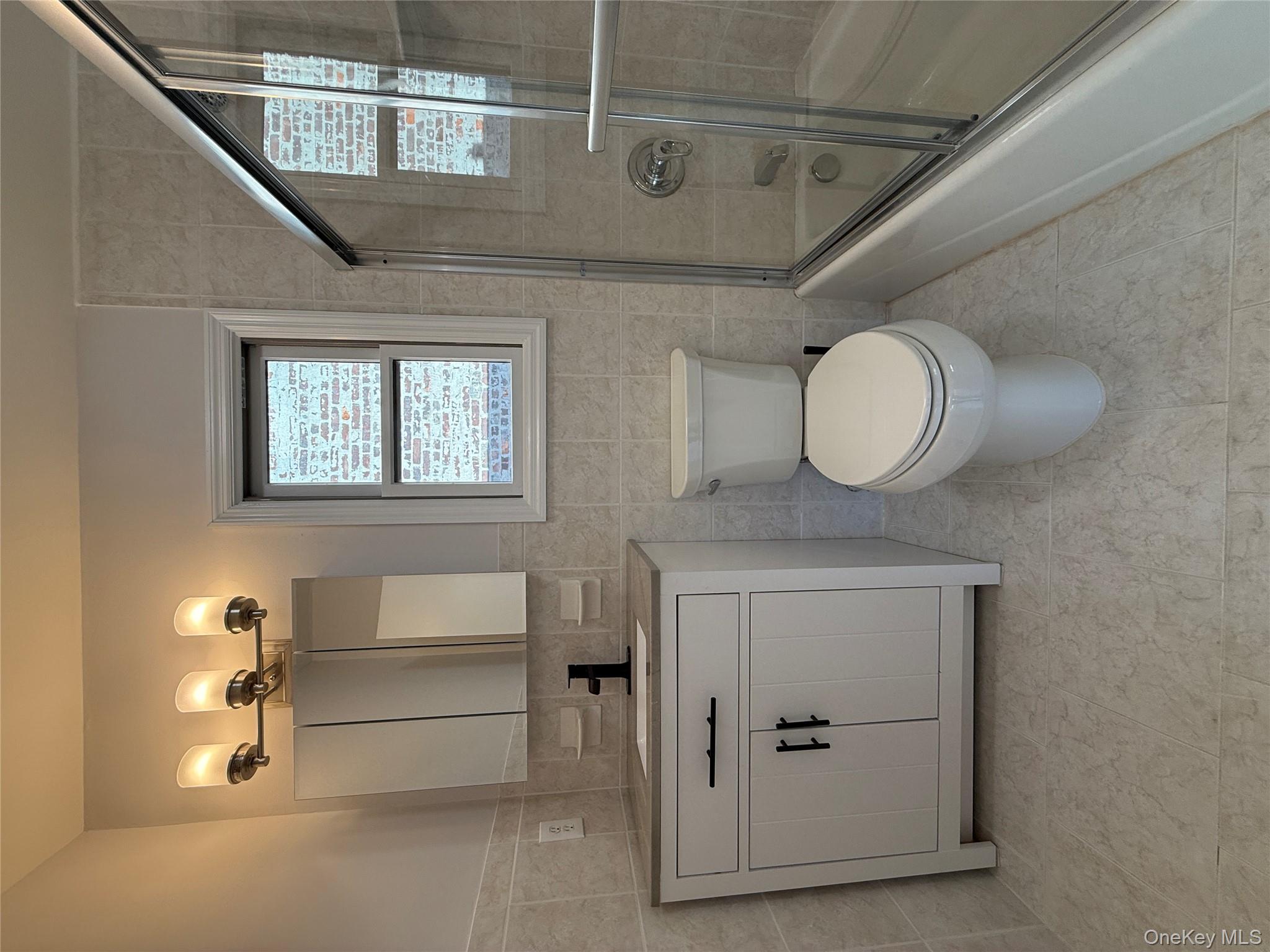 130-09 58th Road Queens, NY 11355 - Photo 16 of 18 Full bath featuring tile walls, bath / shower combo with glass door, vanity, and light tile patterned flooring