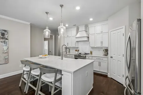 a kitchen with stainless steel appliances granite countertop a stove a refrigerator a kitchen island a sink white cabinets and couches with wooden floor