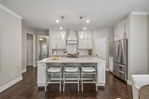 a kitchen with stainless steel appliances granite countertop a dining table chairs refrigerator and sink