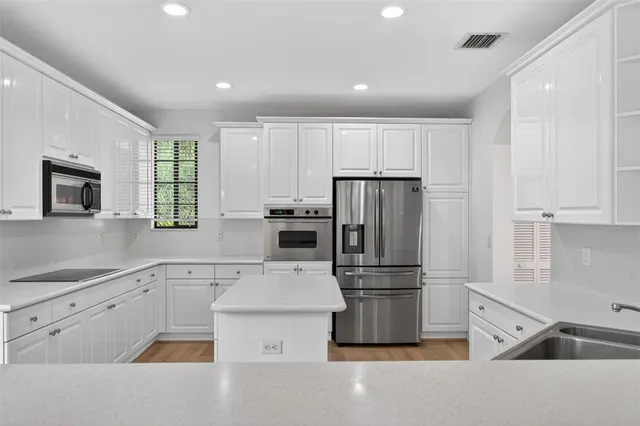 a kitchen with stainless steel appliances granite countertop a stove a sink dishwasher a refrigerator and a dining table with wooden floor