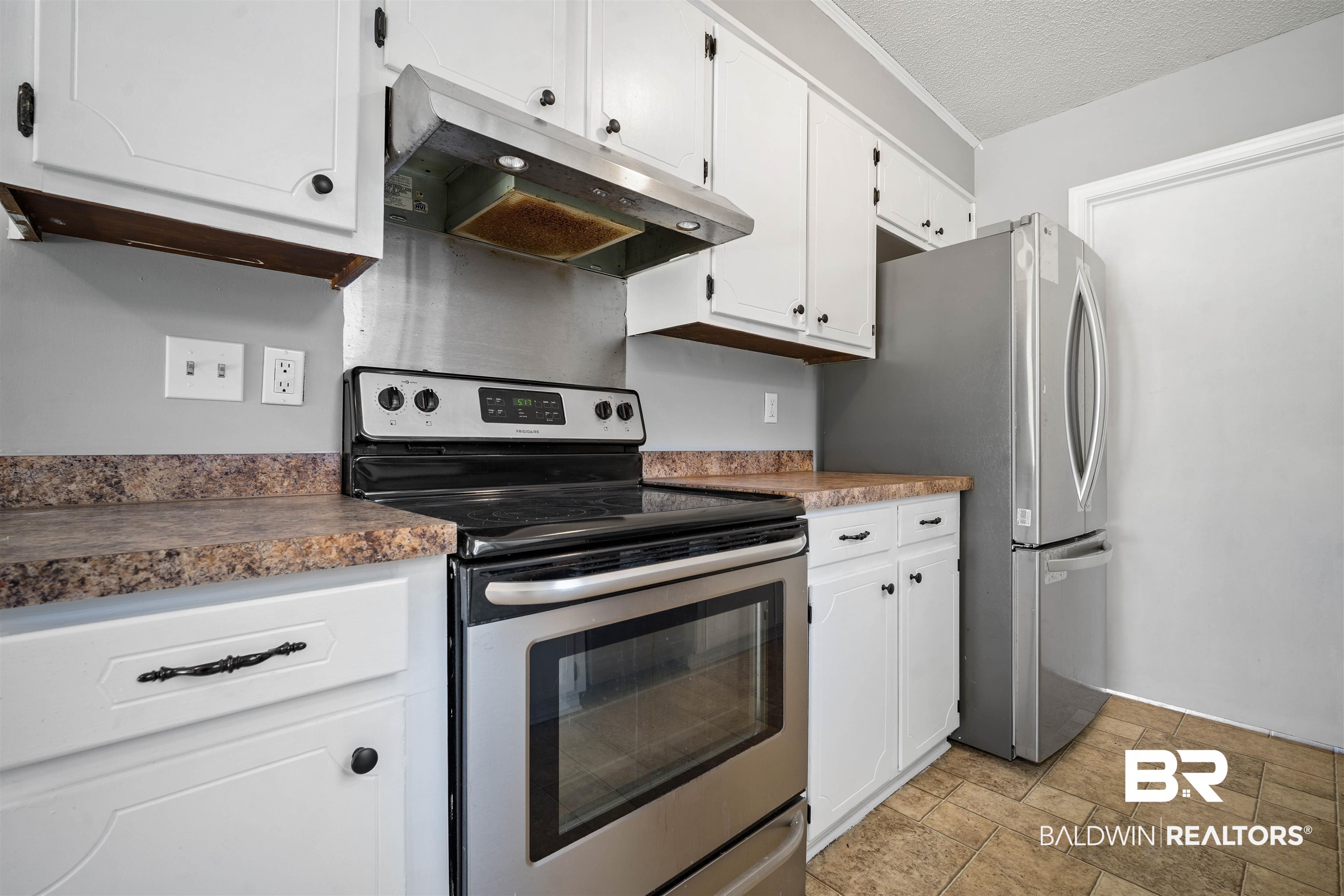 12910 Del Rio Street Grand Bay, AL 36541 - Photo 11 of 26 Kitchen with stainless steel appliances, under cabinet range hood, white cabinets, light stone finish flooring, and a textured ceiling