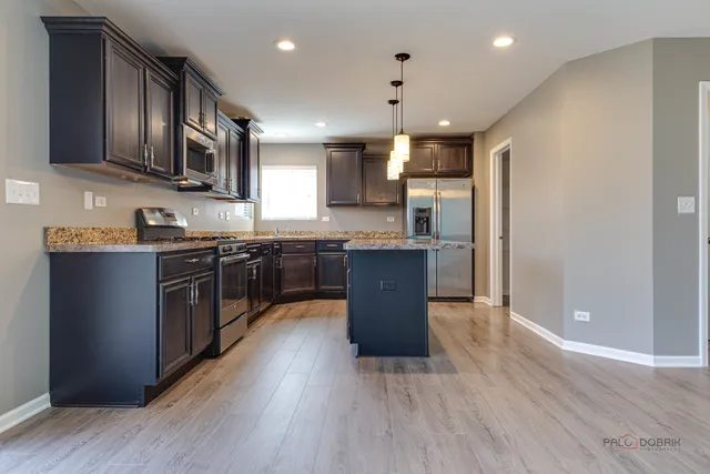 a kitchen with stainless steel appliances granite countertop wooden cabinets a sink a stove a refrigerator and a microwave