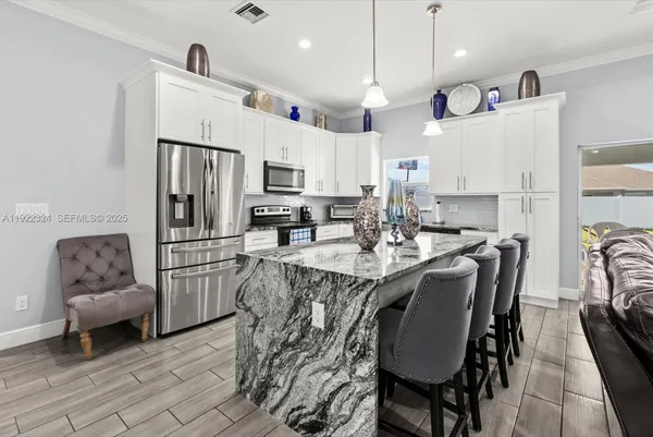 a large kitchen with granite countertop lots of counter top space a sink refrigerator and cabinets