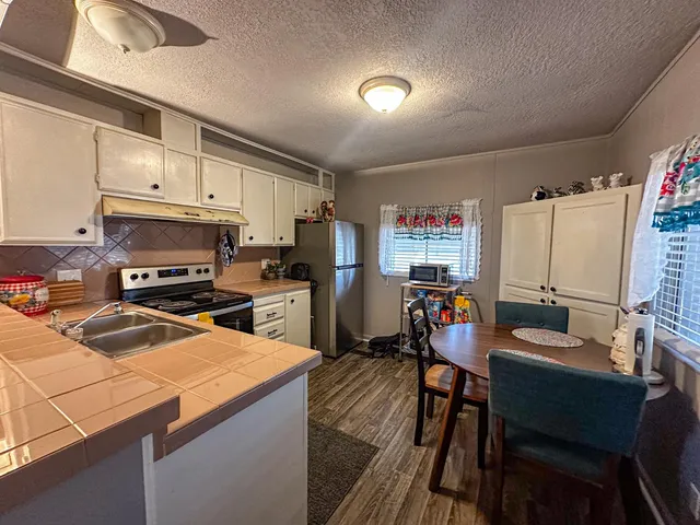 a kitchen with stainless steel appliances a stove a sink a refrigerator white cabinets and chairs