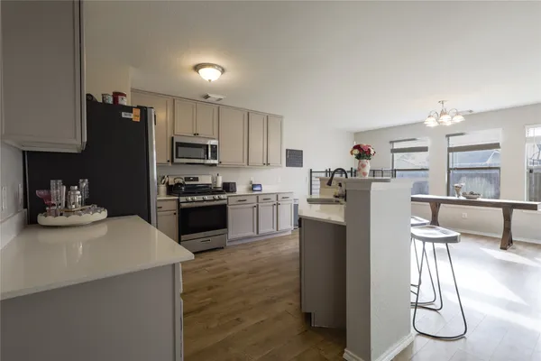 a kitchen with granite countertop a refrigerator oven a sink a dining table and chairs with wooden floor