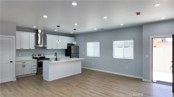 a kitchen with stainless steel appliances granite countertop a stove top oven a sink a refrigerator and white cabinets with wooden floor