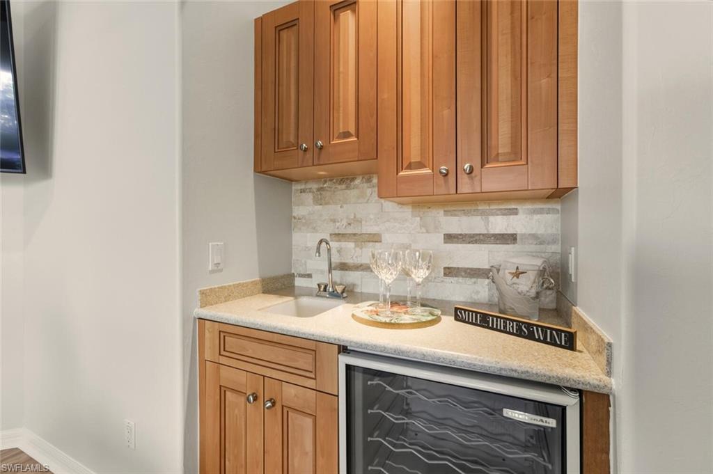 10800 Fieldfair Drive Naples, FL 34119 - Photo 31 of 47 Kitchen featuring brown cabinets, beverage cooler, backsplash, and light stone counters