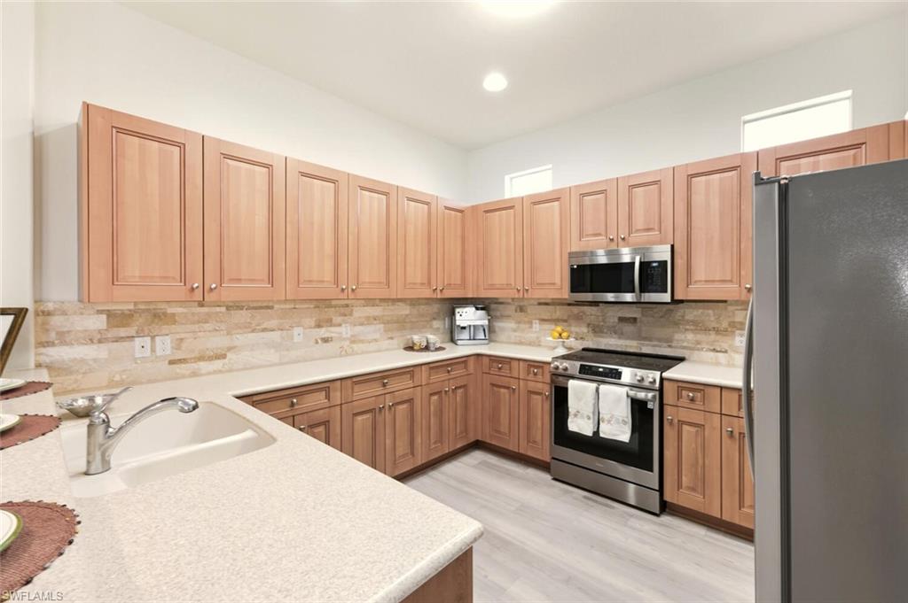 10800 Fieldfair Drive Naples, FL 34119 - Photo 9 of 47 Kitchen with stainless steel appliances, tasteful backsplash, light stone countertops, and light wood finished floors