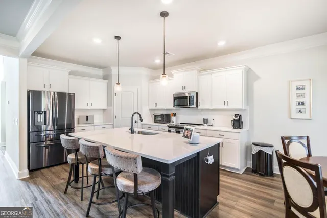 a kitchen with stainless steel appliances a stove a sink a microwave a refrigerator a dining table and chairs with wooden floor