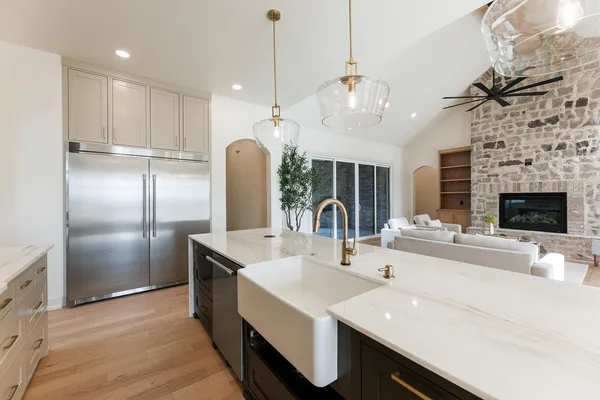 an empty room with a chandelier fan and kitchen view