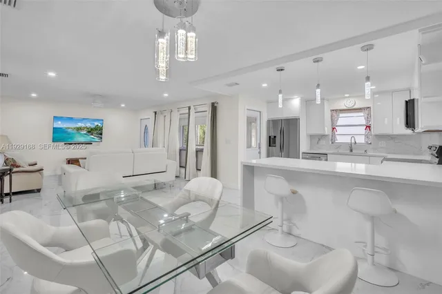 a large white kitchen with stainless steel appliances kitchen island granite countertop a living room and couches with wooden floor