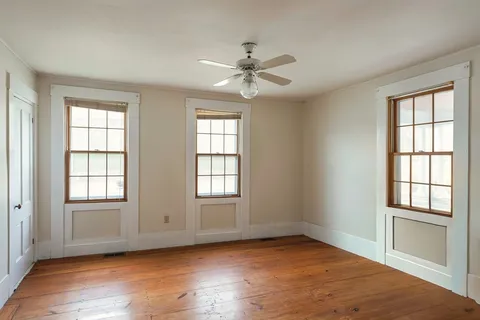 an empty room with wooden floor ceiling fan and windows