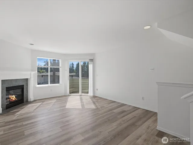 a view of an empty room with wooden floor fireplace and a window