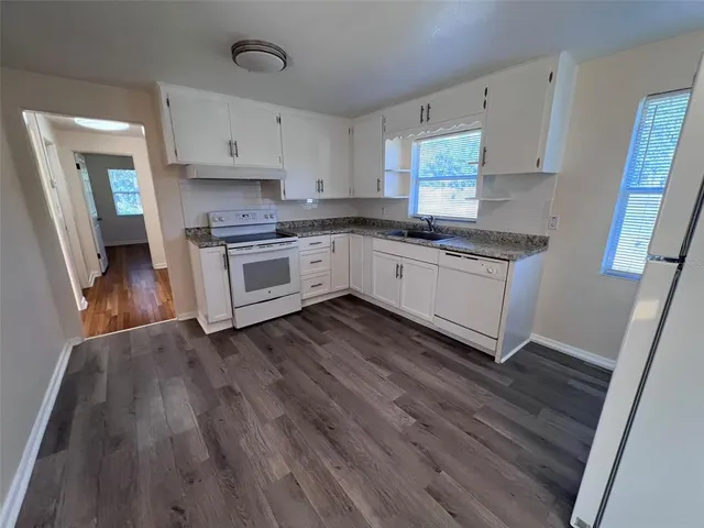 a kitchen with granite countertop wooden floors and white stainless steel appliances