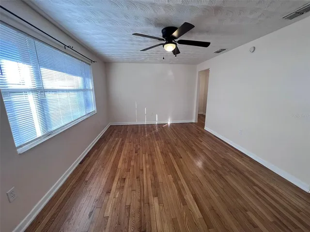 a view of empty room with wooden floor and fan