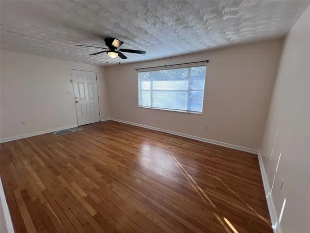 an empty room with wooden floor chandelier fan and windows