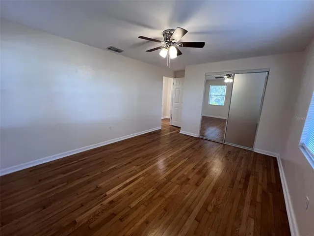 a view of an empty room with wooden floor and a ceiling fan