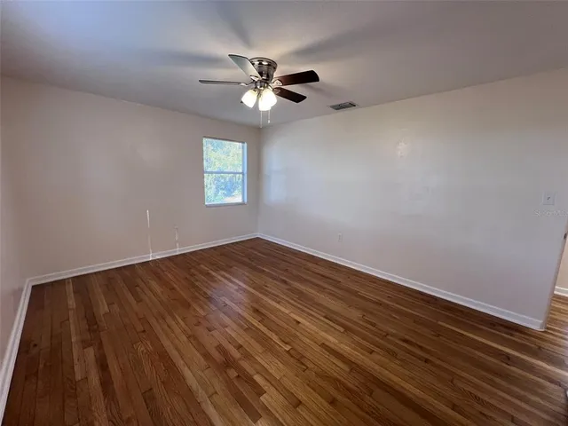 a view of an empty room with wooden floor and a fan