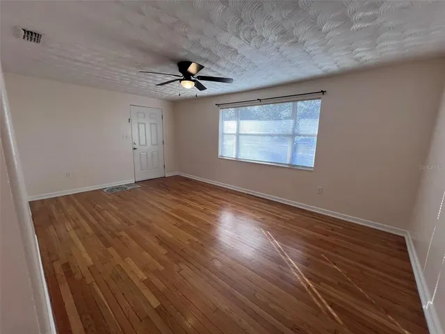 an empty room with wooden floor ceiling fan and windows