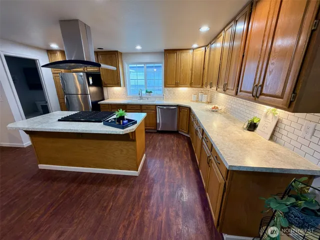 a kitchen with kitchen island granite countertop wooden floors wooden cabinets a sink and appliances