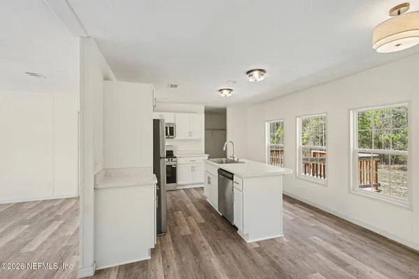 a view of a kitchen with a stove top oven a refrigerator a sink with wooden floor and cabinets