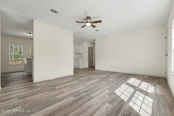 an empty room with wooden floor a ceiling fan and windows
