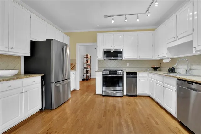 a kitchen with stainless steel appliances a stove a refrigerator a sink and white cabinets with wooden floor