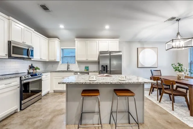 a kitchen with stainless steel appliances granite countertop a stove top oven a sink a dining table and chairs