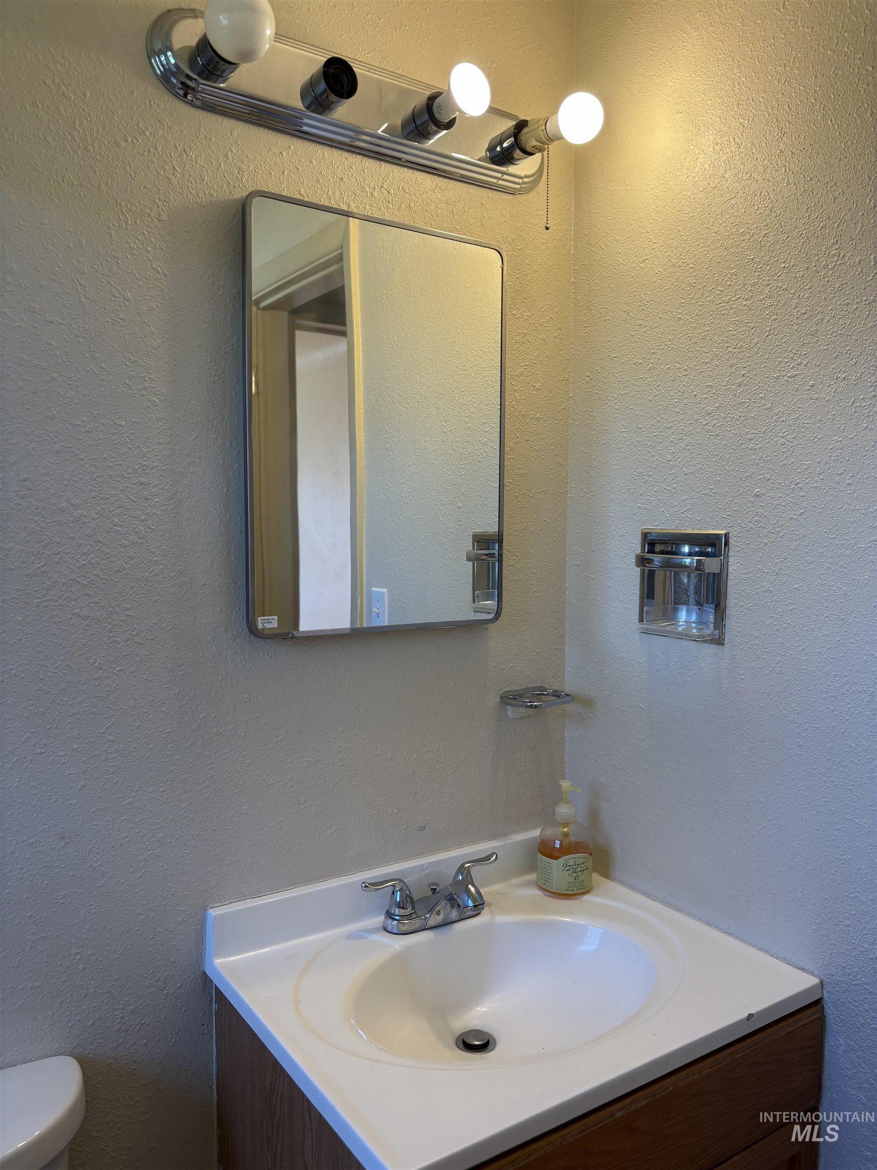 5116 West Morris Hill Road Boise, ID 83706 - Photo 10 of 19 Bathroom vanity featuring a rectangular wall mirror, chrome light fixture, white countertop with integrated sink, and a wood-finish cabinet