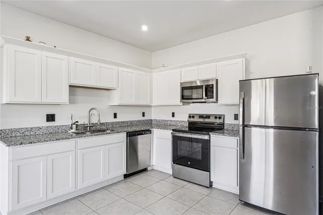 a kitchen with stainless steel appliances granite countertop a refrigerator sink and white cabinets