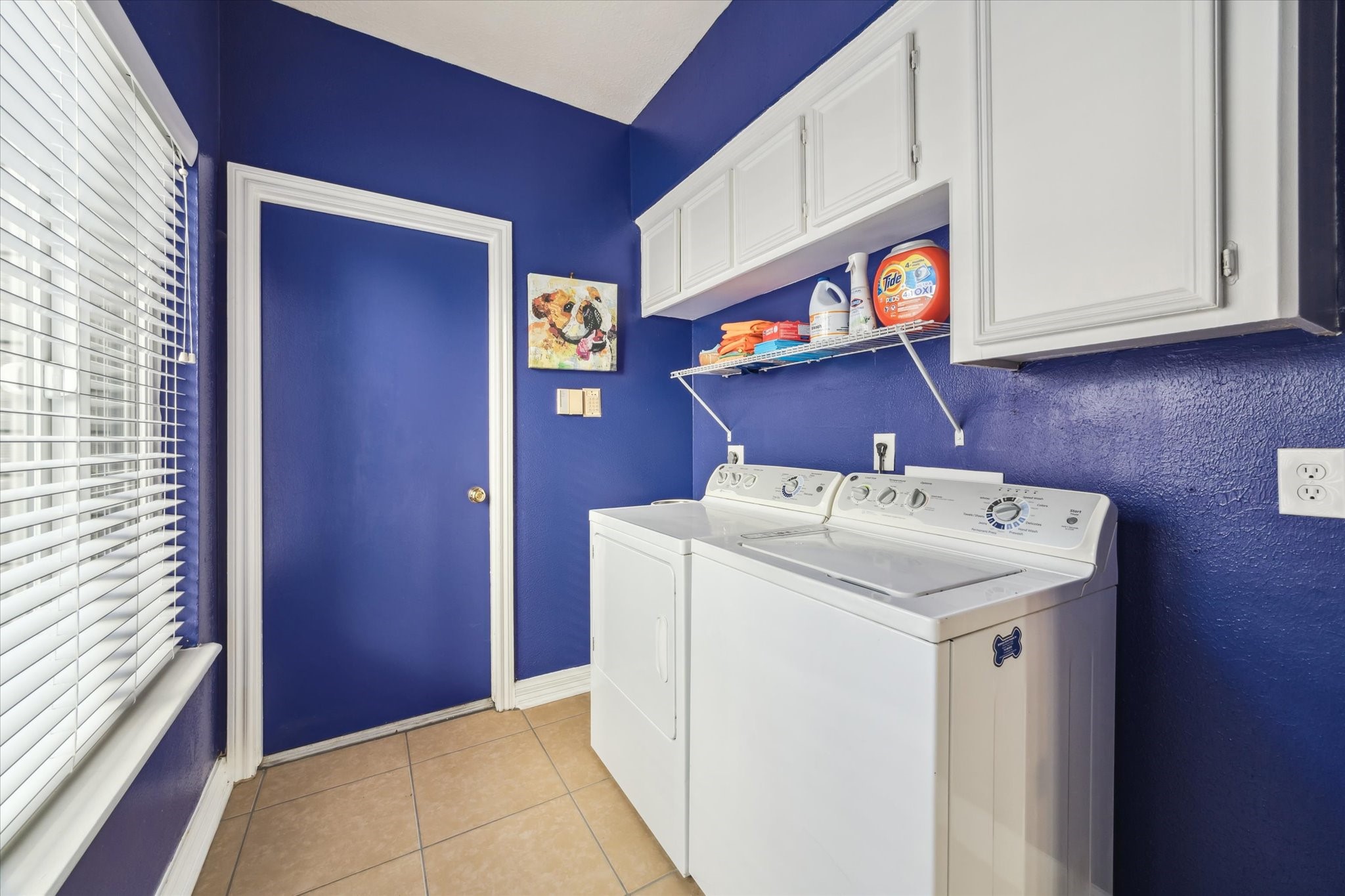 7671 Ameswood Road Houston, TX 77095 - Photo 18 of 23 The laundry room sings with this perky purple paint and fresh white cabinetry. A wall of windows bathes this room in natural light. The door pictured here opens into the oversized attached garage that has plenty of room for cars, a golf cart, storage, and workbench.