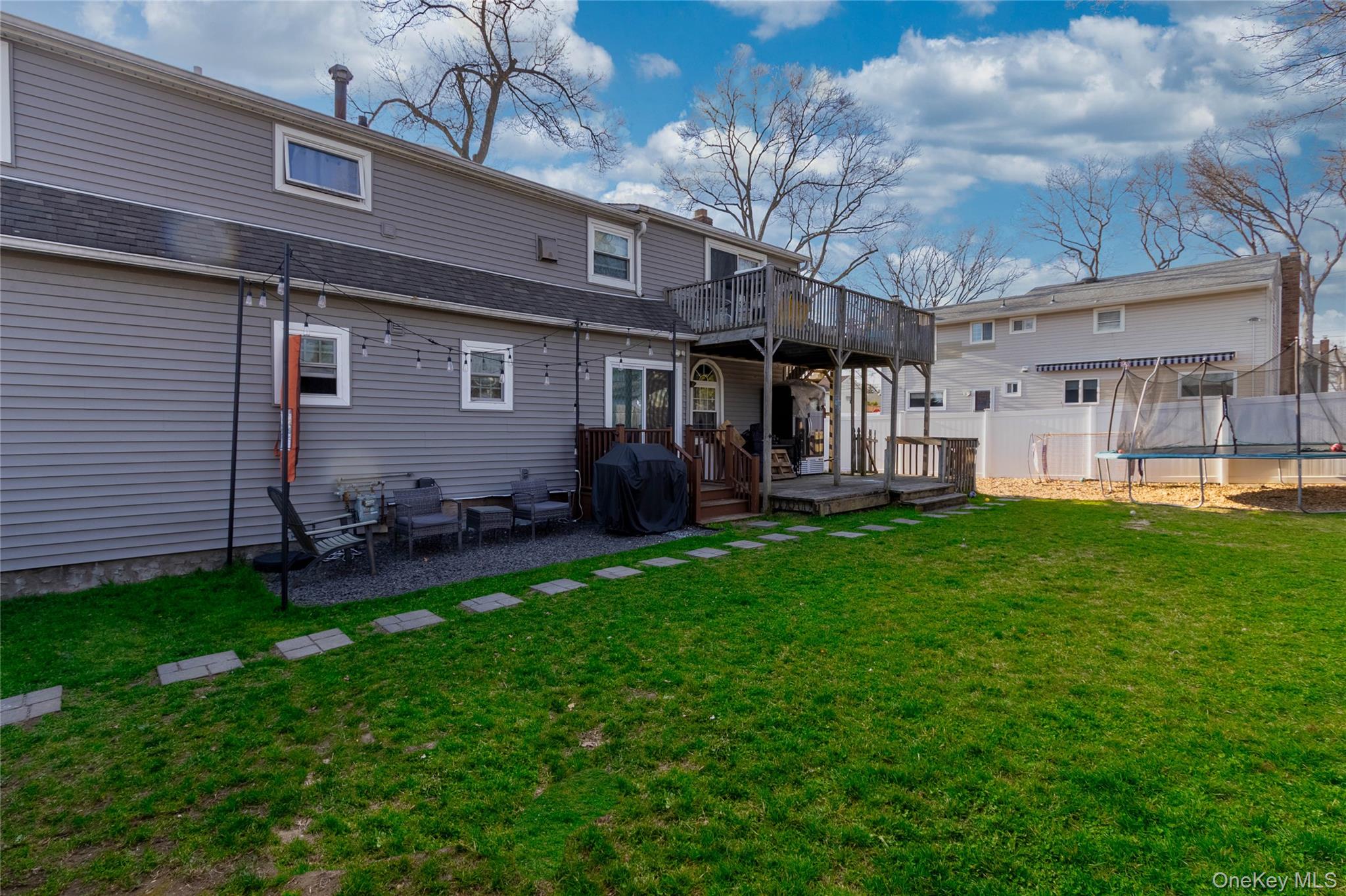 151 Cheltenham Road West Babylon, NY 11704 - Photo 8 of 42 The property features a spacious lawn, a gravel patio area with string lights, and a multi-level wooden deck