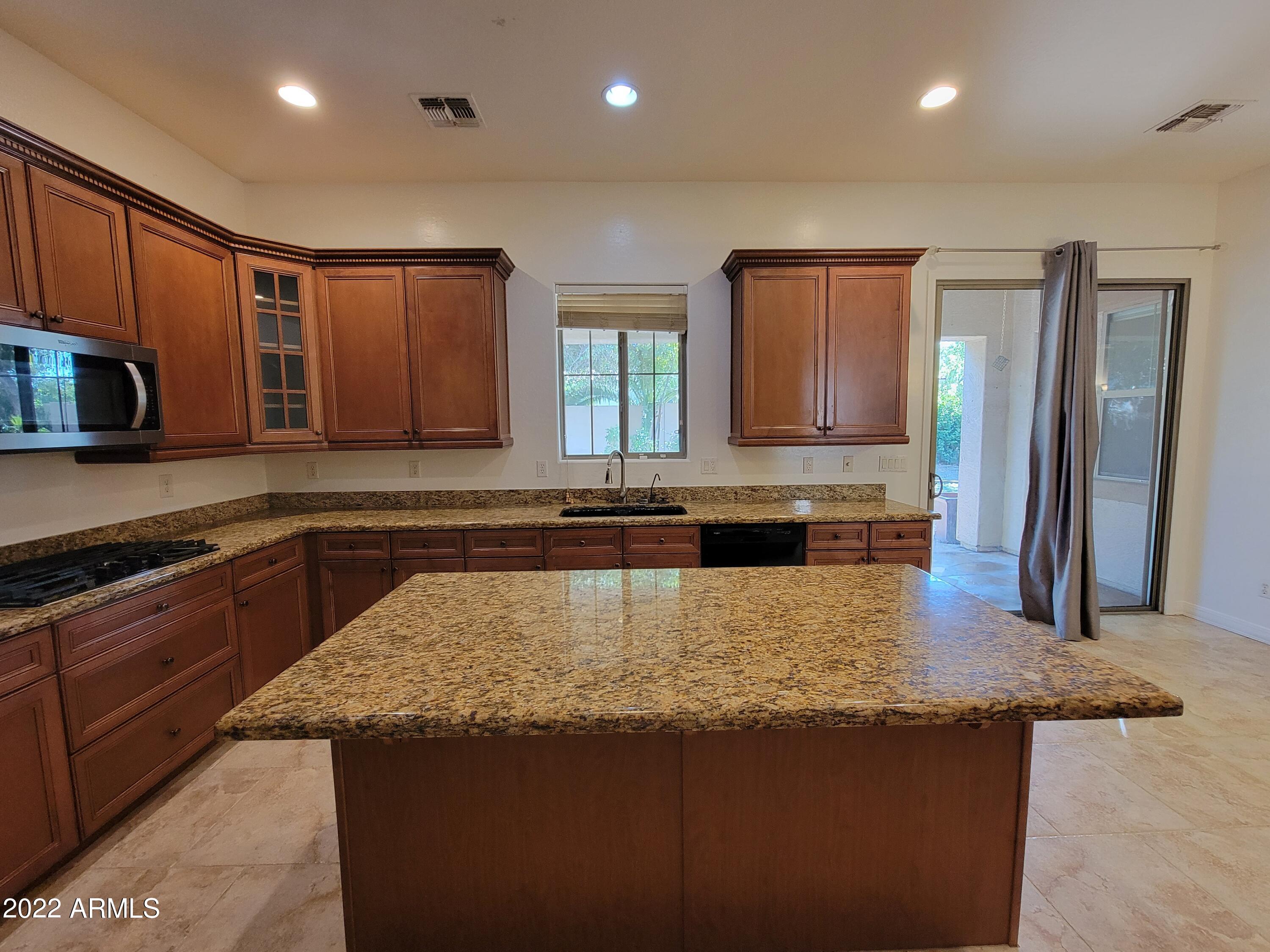 6335 South Roanoke Street Gilbert, AZ 85298 - Photo 10 of 36 a kitchen with kitchen island granite countertop wooden cabinets a refrigerator and a sink