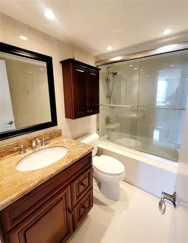 a bathroom with a granite countertop sink a toilet a mirror and bathtub